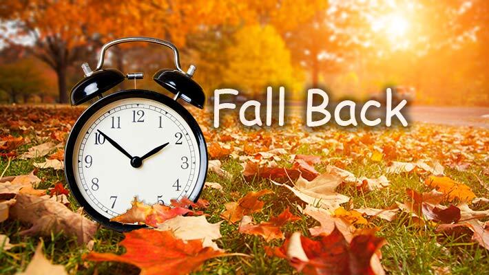 Fall Back. An alarm clock sits on a lawn that is covered in fallen leaves. 