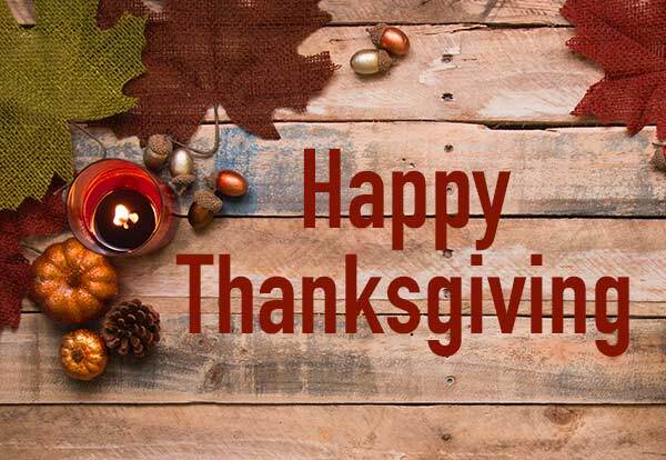 Happy Thanksgiving. Pumpkins, acorns, and leaves are scattered on a wooden table.