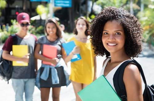 Several students with books and backpacks are walking together on campus.