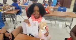 Young lady holding a teddy bear and a card.