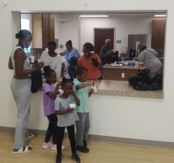 A family standing in front of an opening receiving snacks from assorted people in a kitchen.