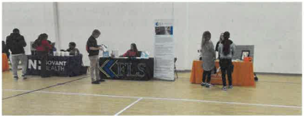 People walking from table to table talking and gathering promotional items. 