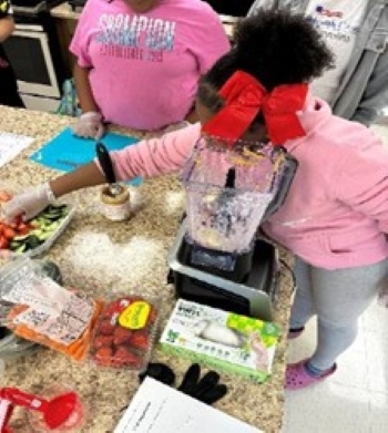 Loung lady reaching for fruits and vegetables to add to the smoothies.