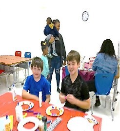 Kids sitting at a table smiling, making arts and crafts.