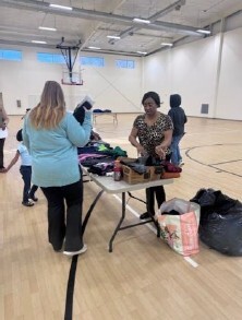 Two women stand around a table with clothes on it.