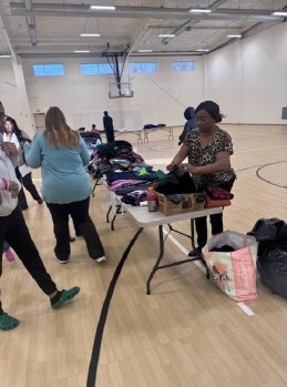 A woman sorting clothes on a table with other women looking at it.