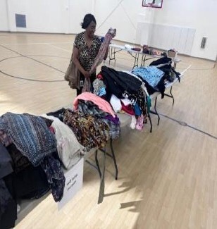 A woman holding a long scarf next to table full of clothes.