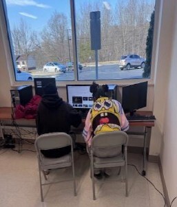 Two children sitting at a computer. One is wearing a spongebob sweater.