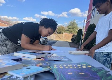 A girl and boy look at books on a table.