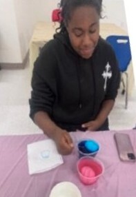 A girl decorating eggs in pink and blue.