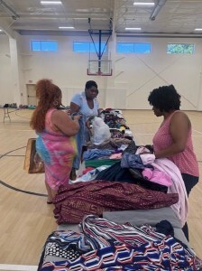 Three women looks at clothes on tables.