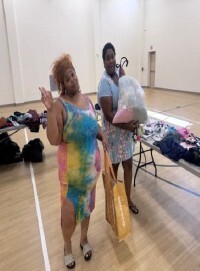 Two women smile for a picture with bags of clothes.
