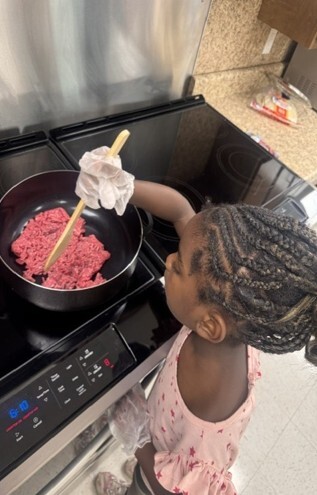 A young girl cooking ground beef on a stove.