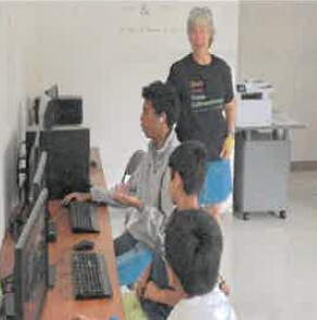 Kids sitting at a table doing things on a computer.