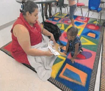 A woman reading to a small child on a colorful rug.