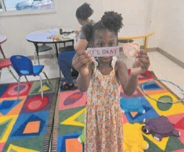 A young girl holding up a sign that says It's okay.