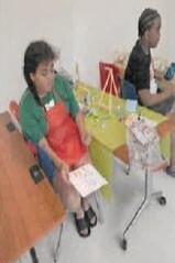 A girl sitting at a table behind a boy doing art.
