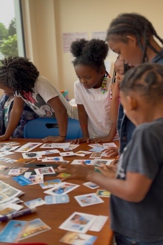 Kids gathered around a table looking at pictures on the table.