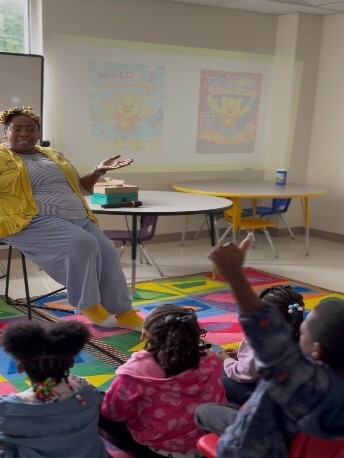 A woman sitting in a chair talking to kids sitting on the floor in front of her.