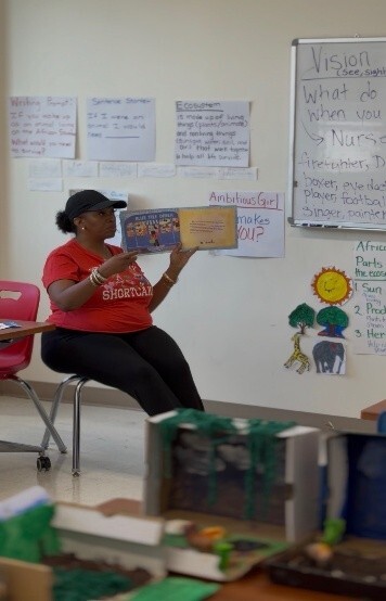 A woman sitting in a classroom reading a book to kids.