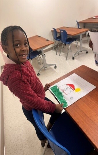 A girl smiling for the photo while holding a drawing.
