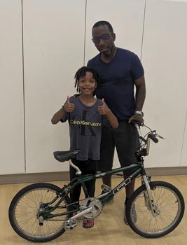 A kid and a man pose for a picture with a bike.